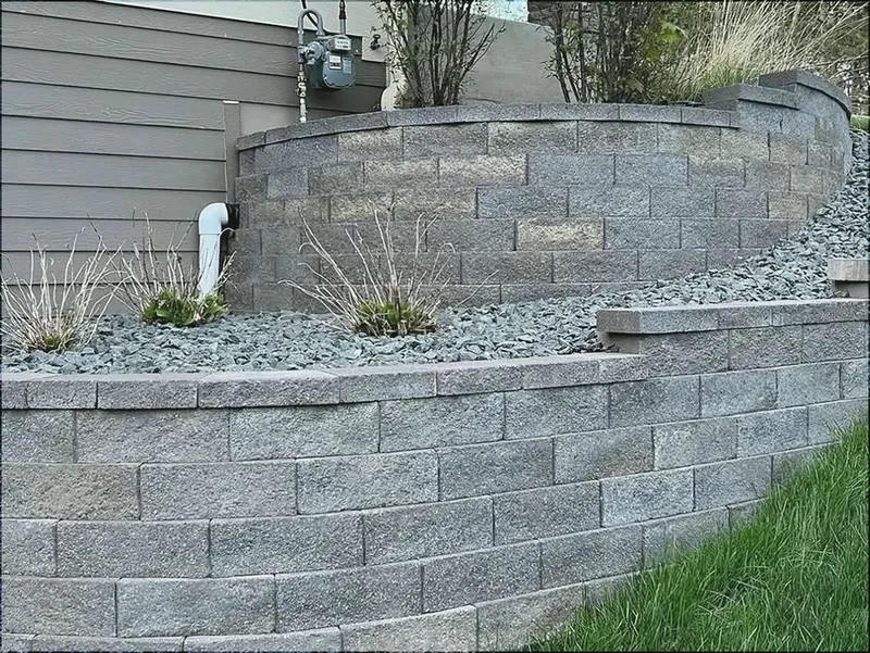 Curved gray block retaining wall with rock beds